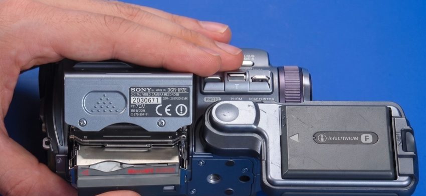 Видеокамера Sony с кассетой MicroMV в руке на синем фоне
